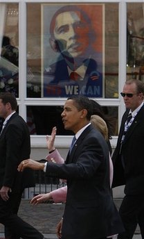 President Barack Obama walks by a large "Yes We Can" Obama campaign poster in a window on the street in the market in Baden-Baden.